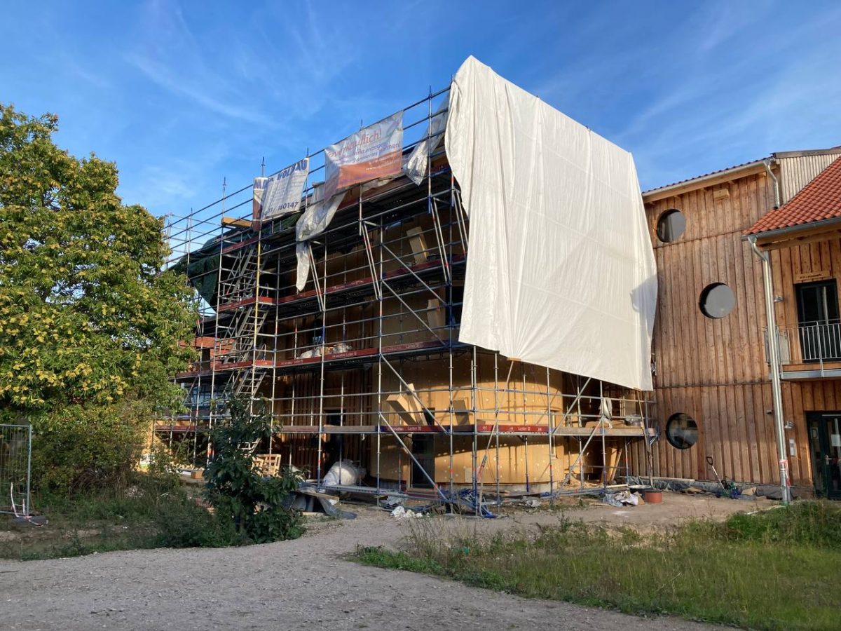 Hinter dem Baugerüst ist schon die beige-braune Dämmung des Silos zu erkennen.
