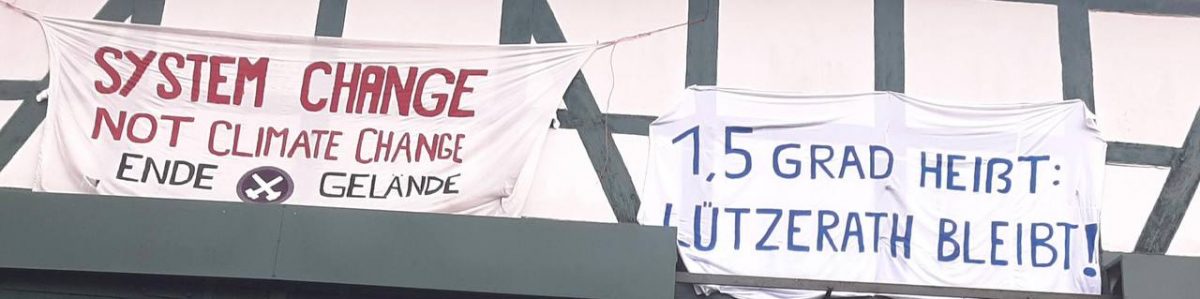 An einer Scheunenwand hängen zwei Banner. "System change, not climate change" steht auf dem einen, auf dem anderen steht "1,5 Grad heißt: Lützerath bleibt!"