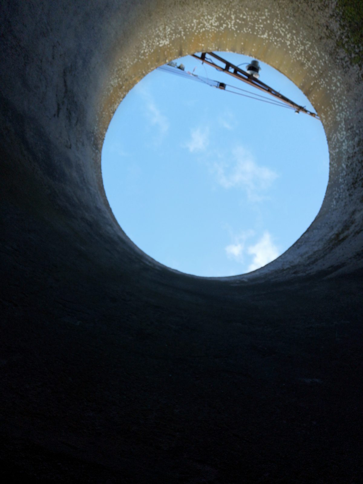 Am Ende eines Betonschachtes wird ein rundes Stück blauer Himmel sowie ein Stück Kran sichtbar.
