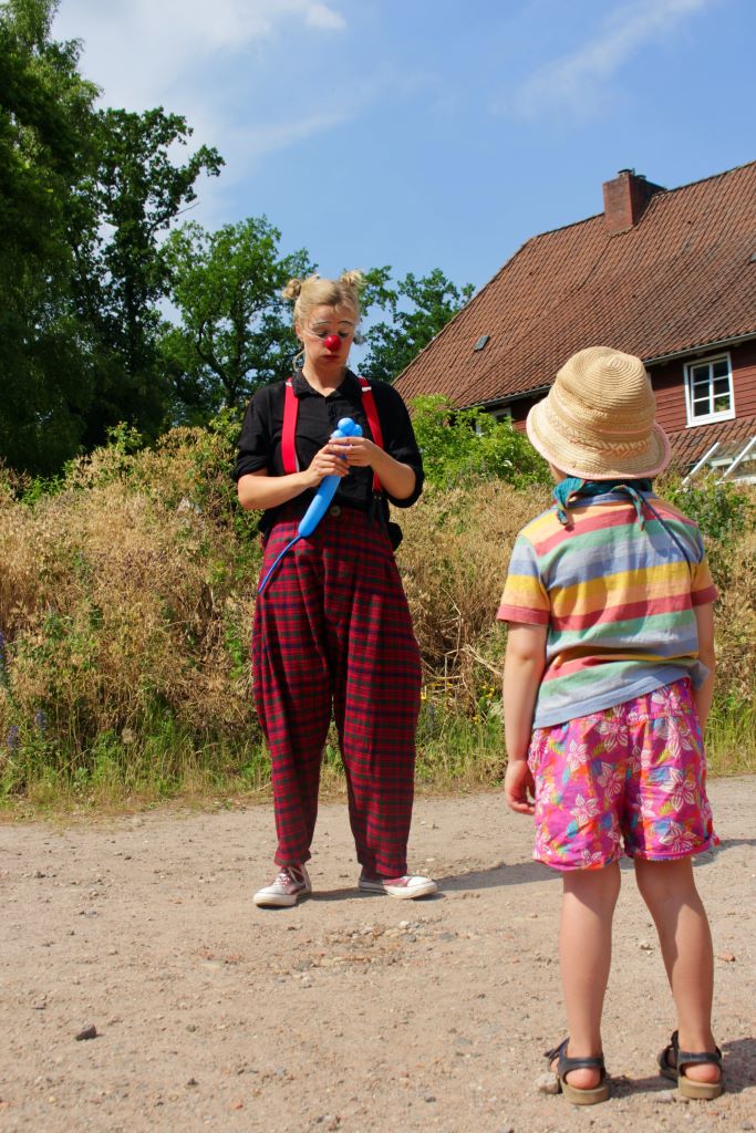 Clown Linn bastelt ein Ballontier. Ein Kind beobachtet sie gespannt dabei.