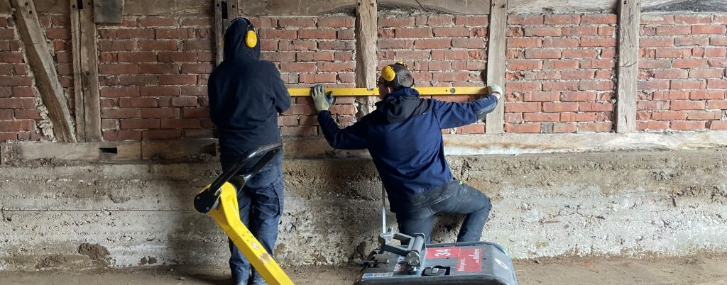 Zwei Personen vor einer Ziegelwand arbeiten mit einer Wasserwaage.