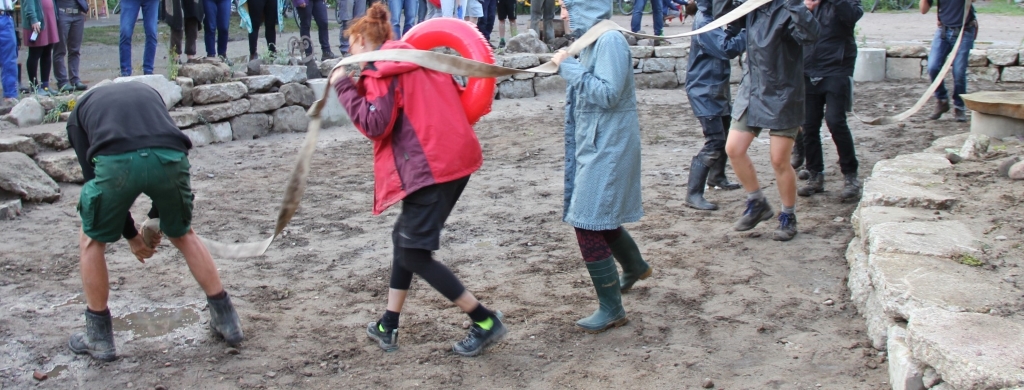 Menschen tragen einen Baumstamm auf sandigem Untergrund.