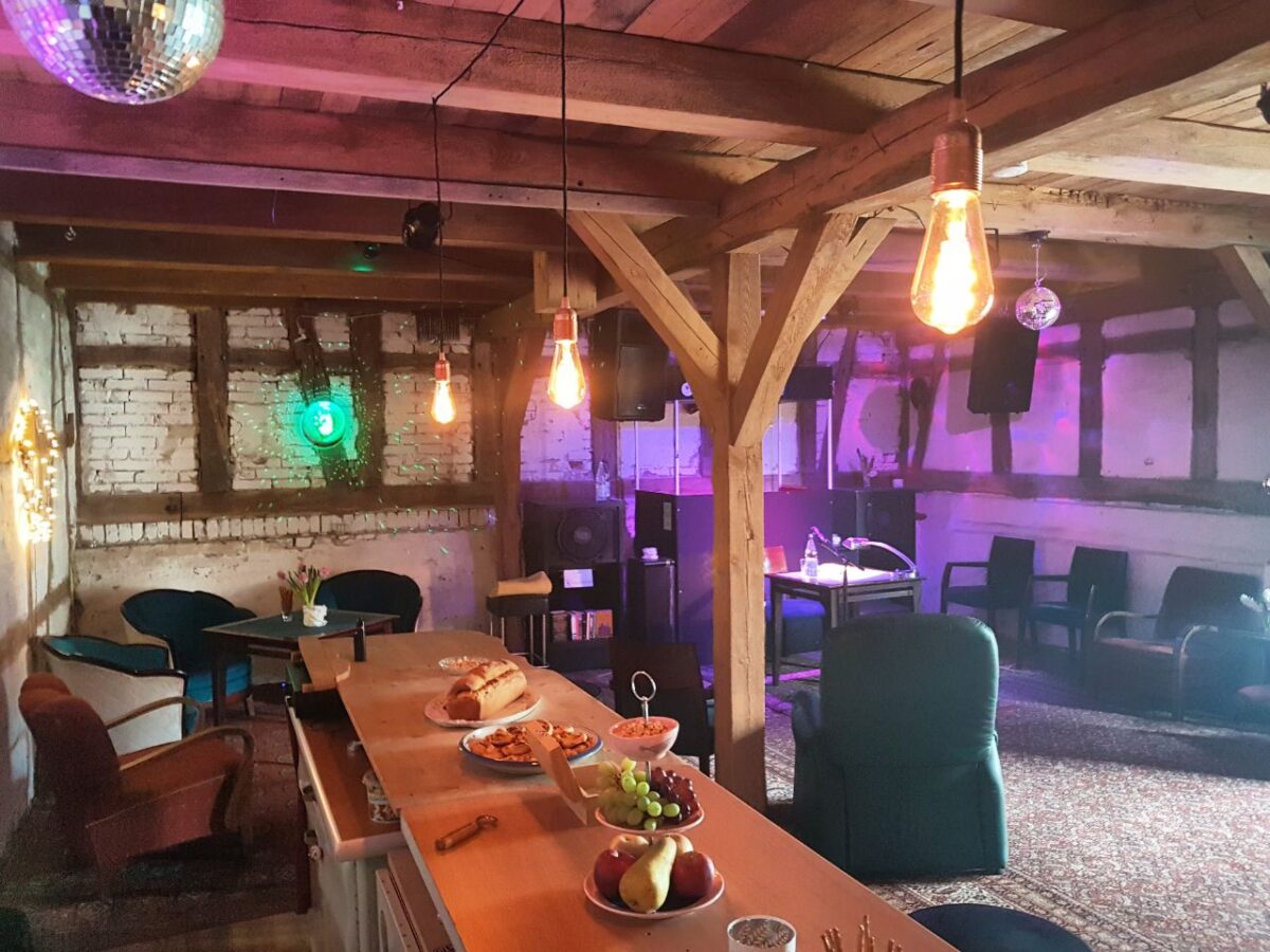 Auf einem Holztresen stehen Teller mit Plätzchen und Früchten. Darüber hängen nackte Glühbirnen von Holzbalken.